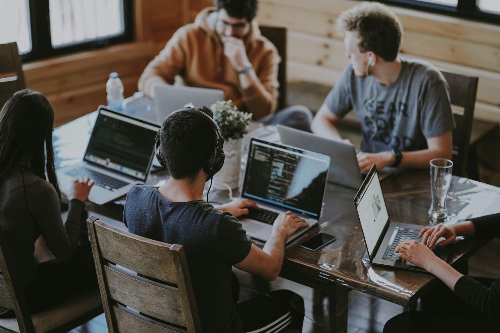Several people working together at a wooden table, each on their own laptop